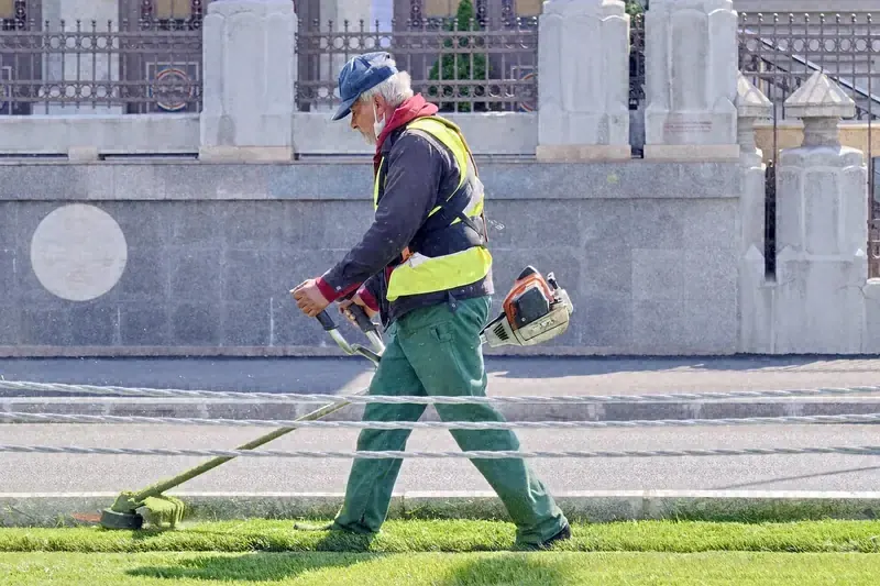 Grounds worker in a safety vest string trimming grass along a curb